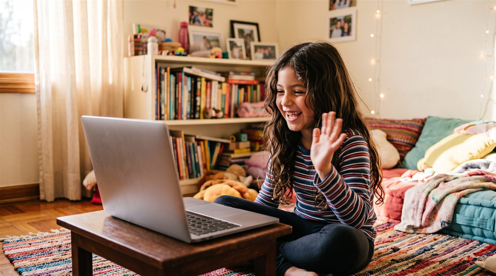 Niña latinoamericana sonriendo frente a la pantalla de una laptop mientras saluda a otros niños en una clase de japonés en vivo