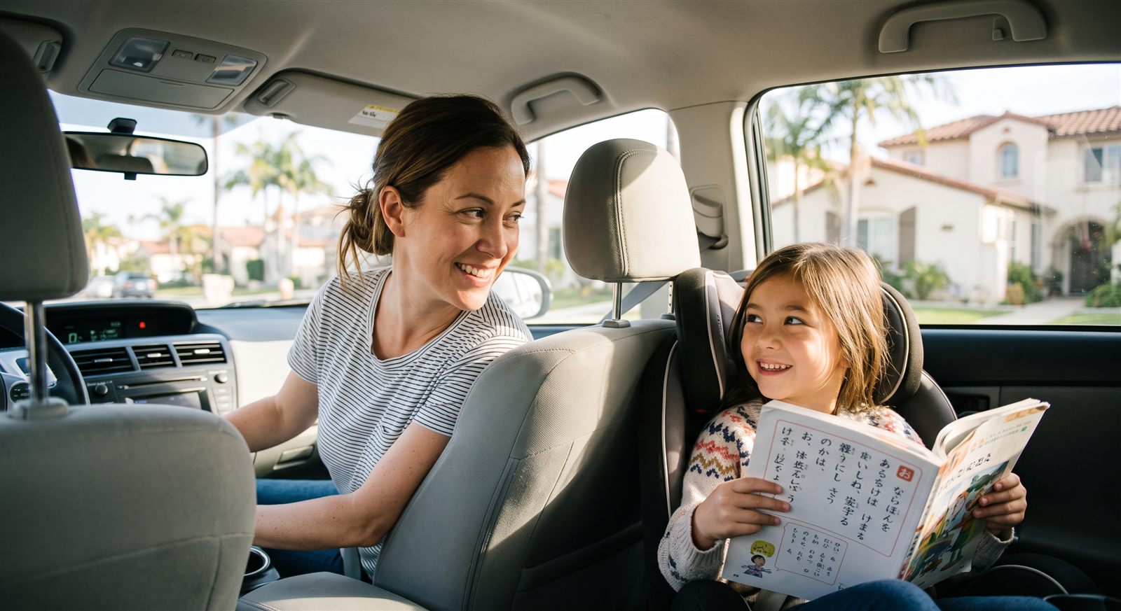 A mother glances back at her daughter, holding a Japanese textbook, in the back seat of a car in Southern California